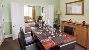 A dining area with a wooden table set for six, surrounded by black chairs. A chandelier hangs from the ceiling, and a wooden cabinet with glassware is to the right. - Oakhurst (Keswick)