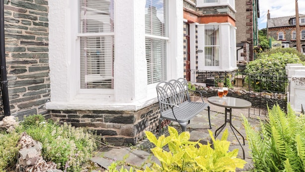 A corner building with a stone facade, white-painted windows, and a small outdoor seating area with a table and chairs. - Oakhurst (Keswick)