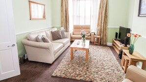 A living room with a beige sofa, a wooden coffee table, and a television on a wooden stand. - Oakhurst (Keswick)