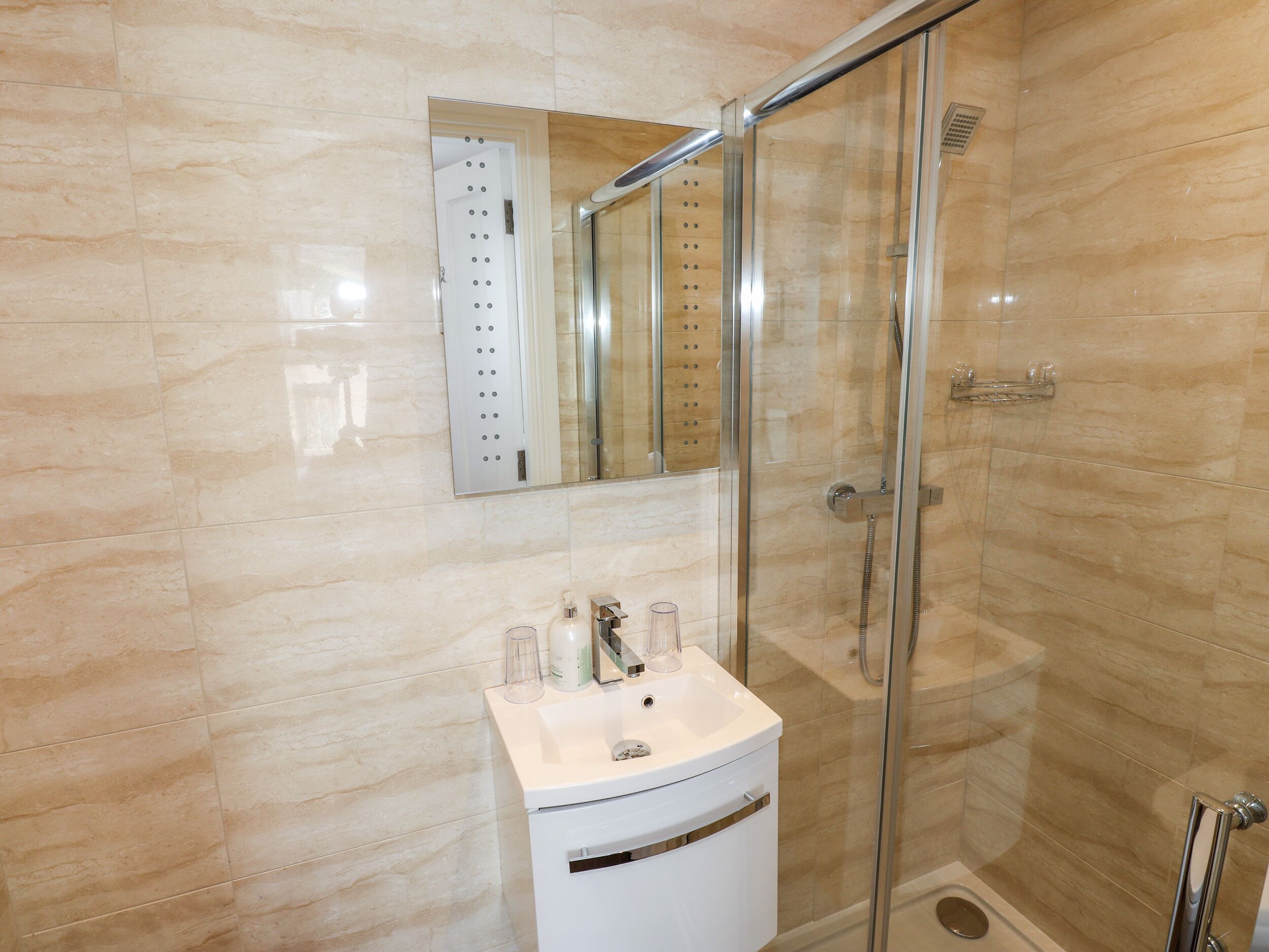 Une salle de bain moderne avec une douche à parois de verre, un lavabo blanc et un miroir au-dessus.