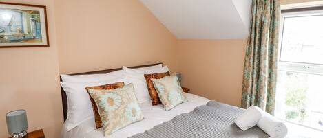 A neatly made bed with floral pillows, a bedside lamp, and a window with curtains.