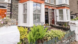 A traditional terraced house with a bay window, stone facade, and a small garden with plants and a table. - Oakhurst (Keswick)