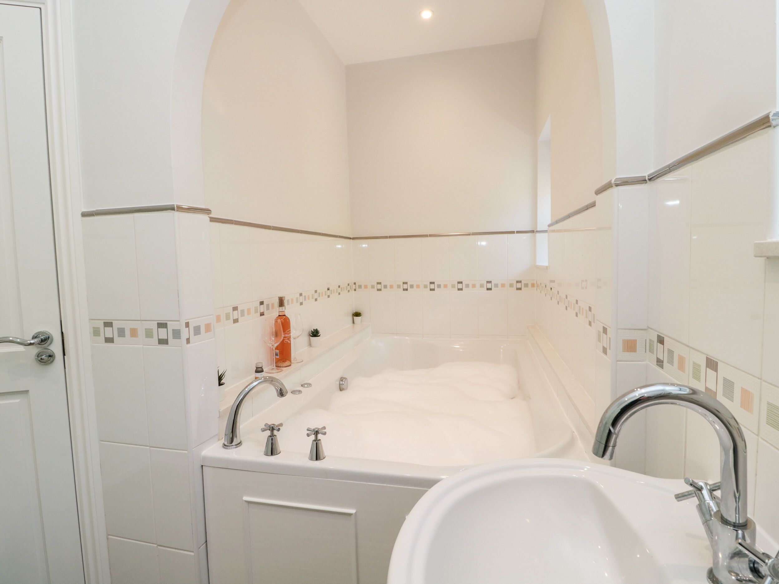 A bathroom with a large bathtub, a sink, and a shower. There is a shelf with decorative items and a potted plant.
