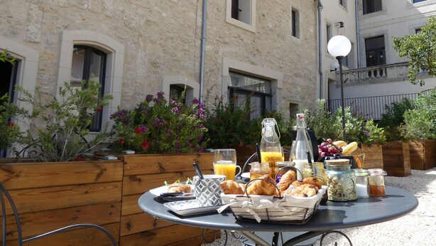 An outdoor breakfast setup with a table, food, and drinks in front of a stone building with windows and a balcony. - Luxury Suite with Spa - La Nébuleuse (Vendres)