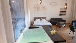 A modern bathroom with a large bathtub, a small table with candles, and a seating area with a sofa and chairs. - Luxury Suite with Spa - La Nébuleuse (Vendres)