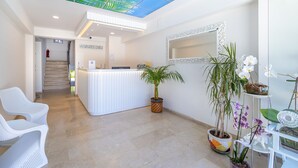A reception area with a modern design, including a reception desk, white chairs, potted plants, and a ceiling with a leaf pattern. - Princess Kinli Suites Hotel (Marmaris)