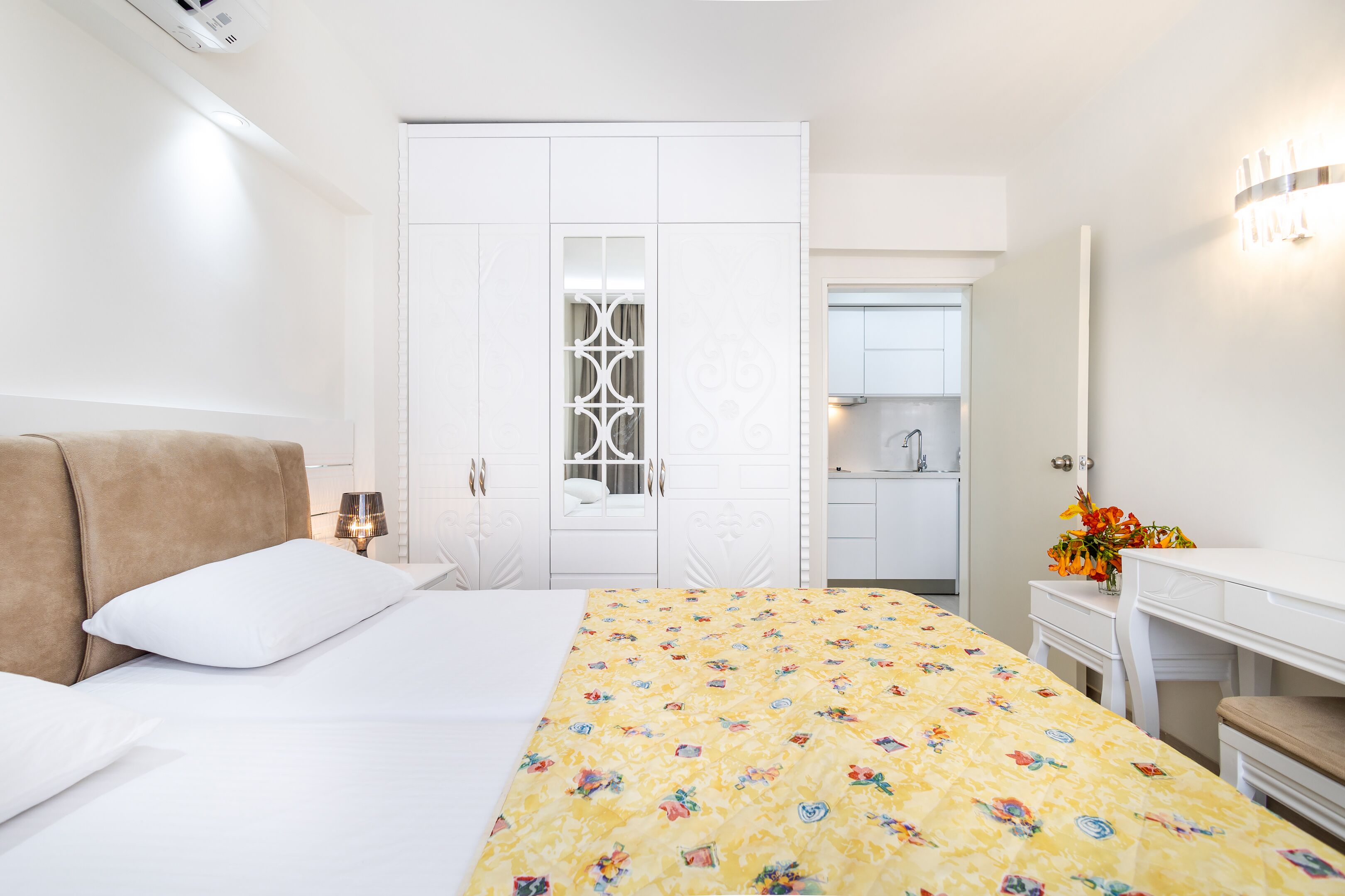 Ein Hotelzimmer mit Bett, Nachttisch, Lampe, Kleiderschrank, Schreibtisch und Spiegel.