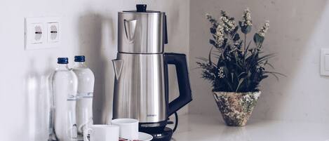A kitchen with a coffee maker, two water bottles, a potted plant, and a white countertop.
