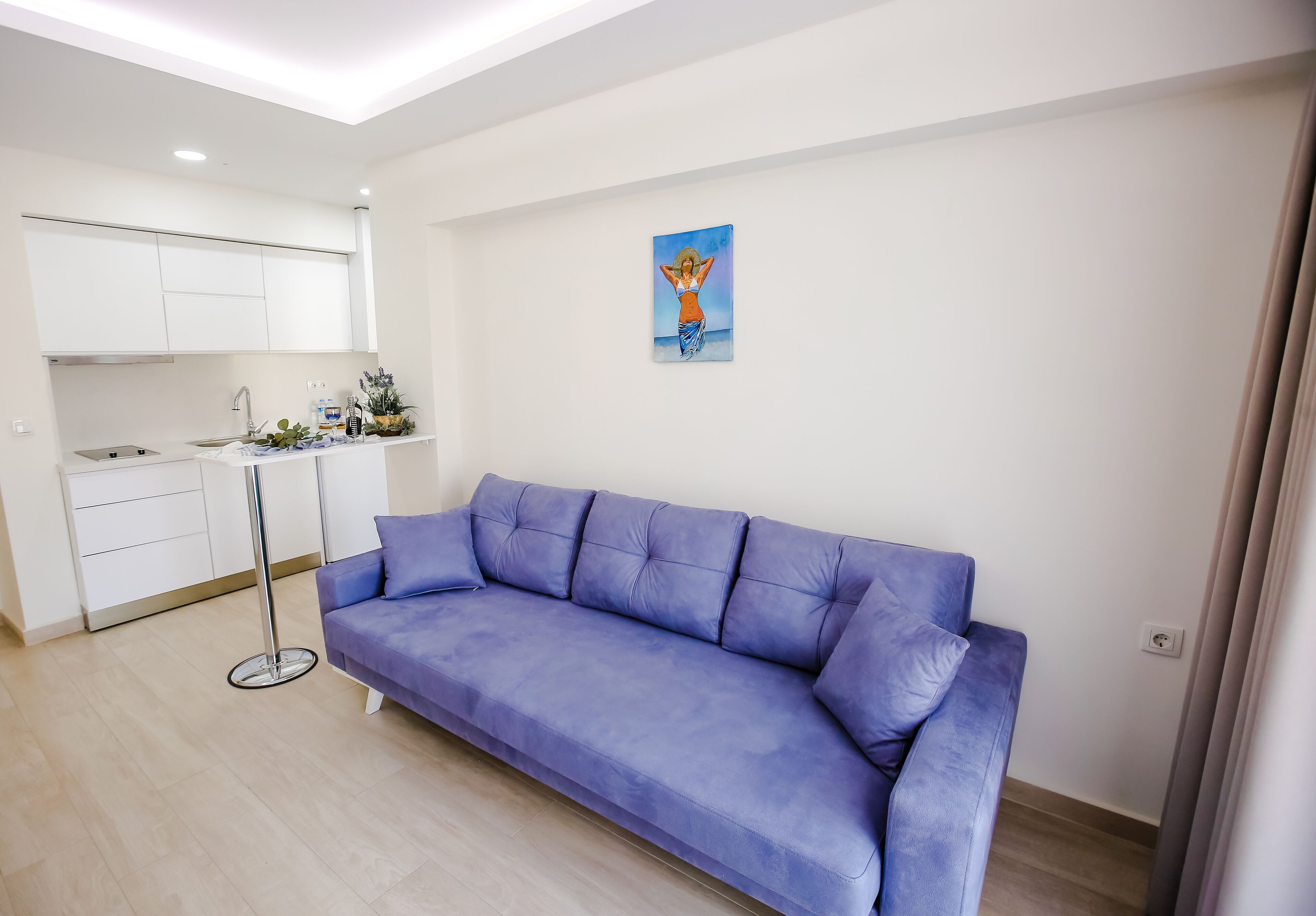 Un salon moderne avec un canapé bleu, un petit coin cuisine et un tableau accroché au mur.