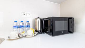 Una cocina americana con un microondas negro, una cafetera de acero inoxidable y varias botellas de agua sobre una encimera blanca.