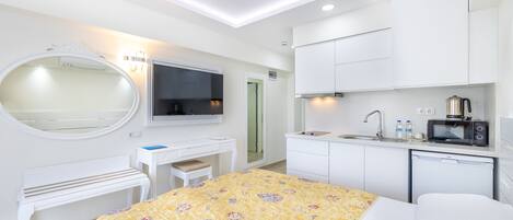 A hotel room with a bed, a desk, a mirror, a television, a kitchenette, and a bathroom.