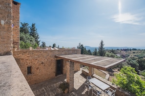 A stone building with a pergola and outdoor seating area, overlooking a scenic landscape.
