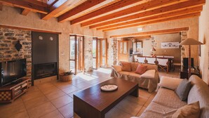 Un salon spacieux doté d’une cheminée, de poutres en bois, de murs en pierre et d’un coin salon confortable.