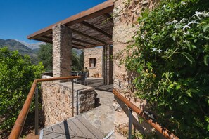 A stone building with a wooden pergola, a stone staircase, and a view of mountains.