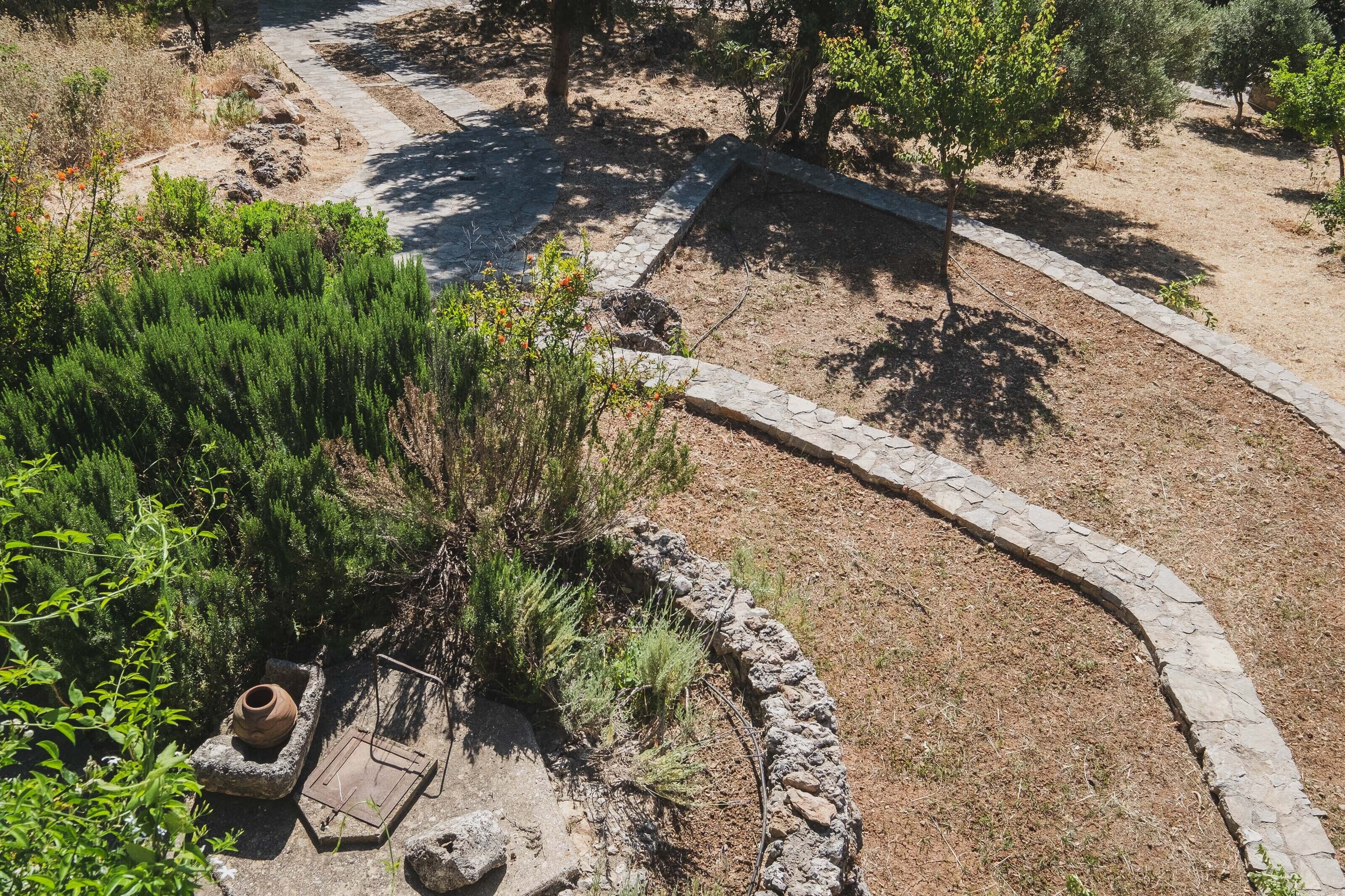 A landscaped garden with a stone pathway, a small seating area with a pot, and various shrubs.