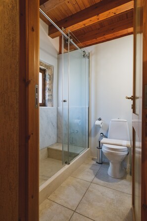 A bathroom with a glass shower enclosure, a toilet, and a marble-tiled floor.