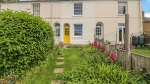 A two-story building with a yellow door, a garden with stepping stones, and a wooden fence. - Bedford Terrace (Bridport)