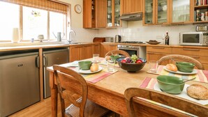 A kitchen with wooden cabinets, a dining table set with green bowls, and a window with blinds. - Bedford Terrace (Bridport)