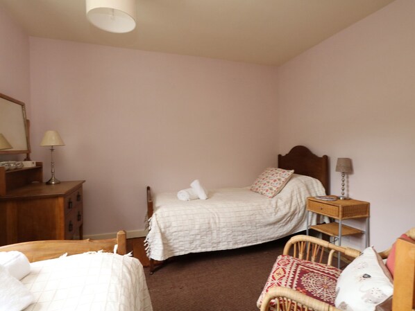 A bedroom with a bed, a wooden nightstand, a wicker chair, and a dresser. - Bedford Terrace (Bridport)