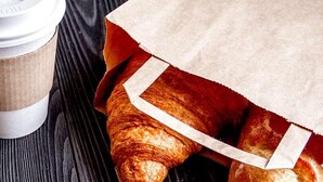 A coffee cup and a paper bag with a croissant on a wooden surface.