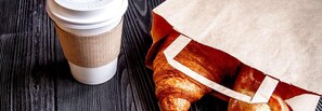 A coffee cup and a paper bag with a croissant on a wooden surface. - Signature Inn Santa Clara (Santa Clara)