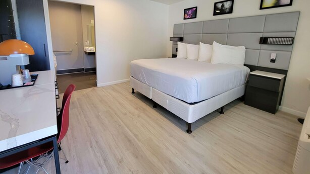 A modern hotel room with a bed, bedside tables, a desk with a lamp, and a chair.
