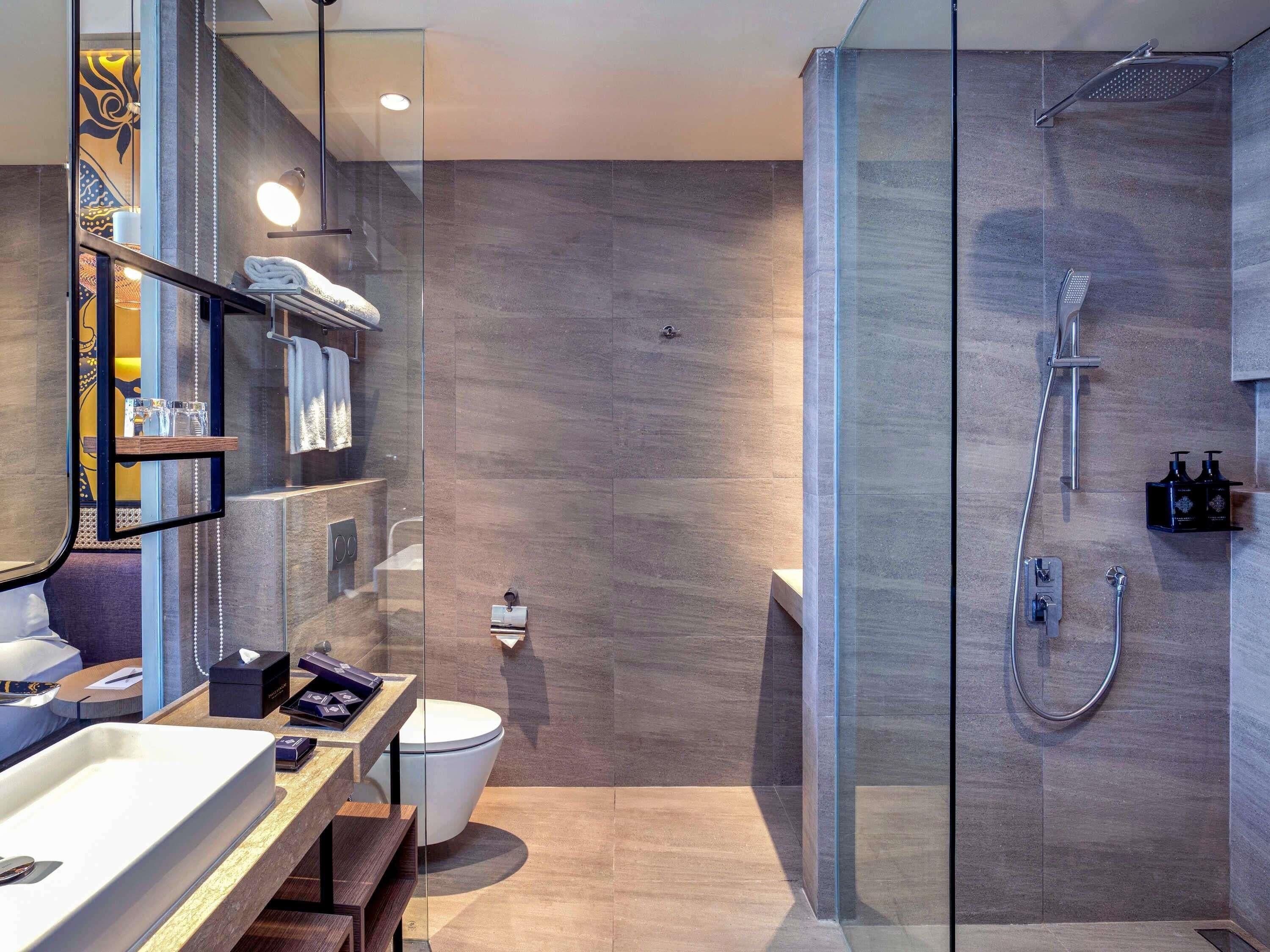 Un baño moderno con cabina de ducha de vidrio, inodoro y tocador con espejo y estantes.