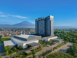 Un hotel moderno con un llamativo letrero de 'Grand Mercure', rodeado de exuberante vegetación y vistas a una montaña.