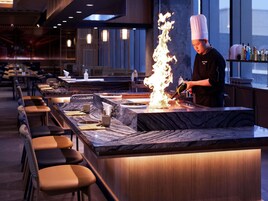 Un chef realiza un flambé en una barra con una larga barra y zona de asientos.