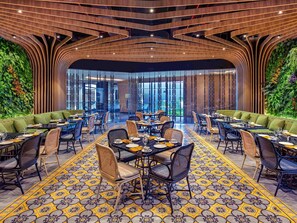 A modern restaurant with a central dining area, green upholstered seating, and a patterned floor. - Grand Mercure Malang Mirama (Malang)
