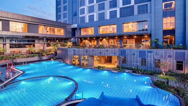Un hotel moderno con una amplia piscina al aire libre, varias zonas de restauración y un edificio alto con numerosas ventanas.