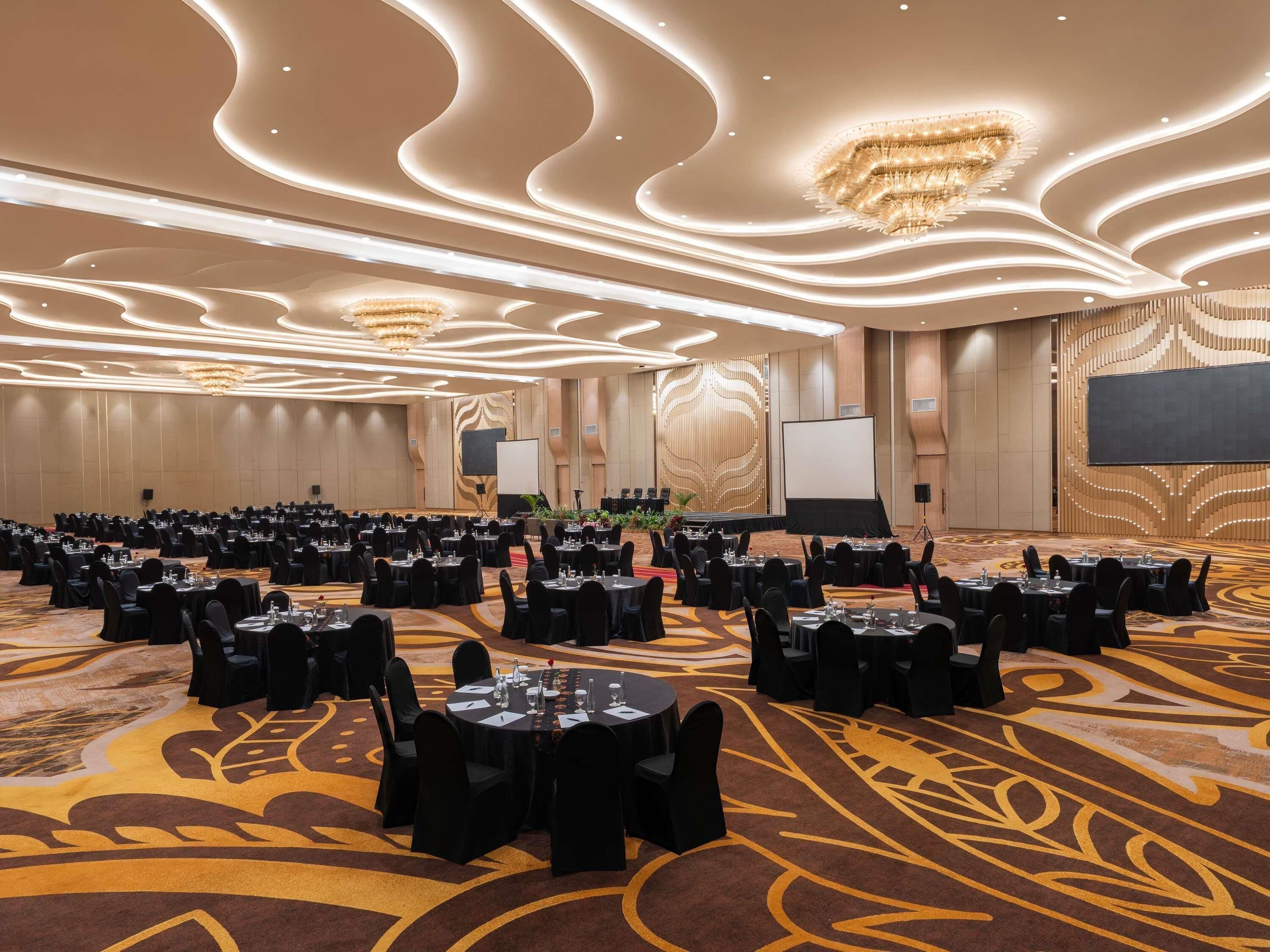 A large conference room with round tables, black chairs, and a carpeted floor.