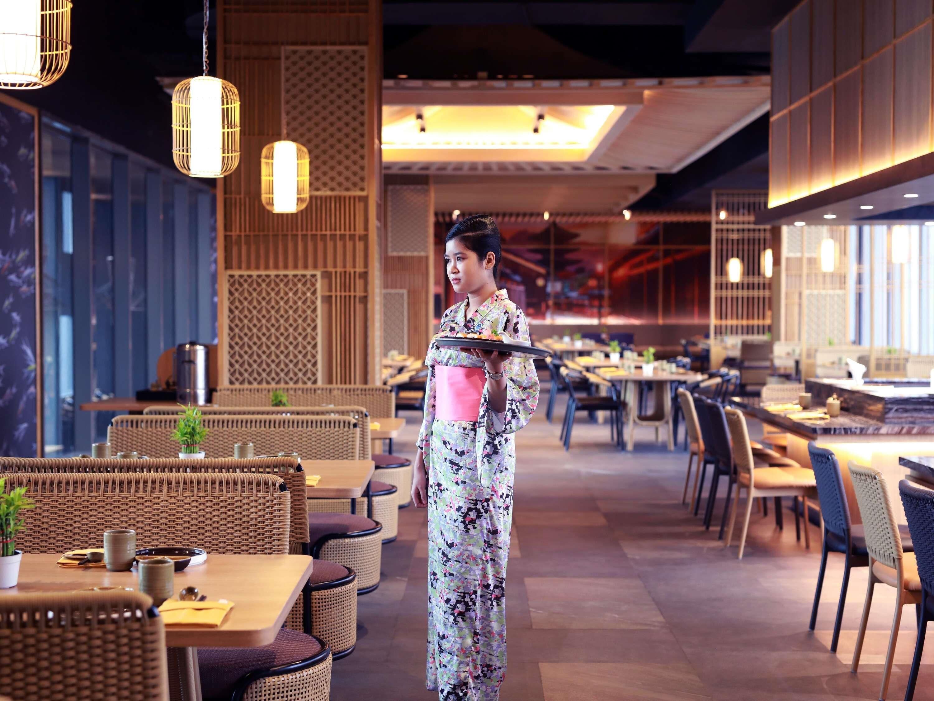 A restaurant interior with wicker furniture, hanging lights, and a person in traditional attire.