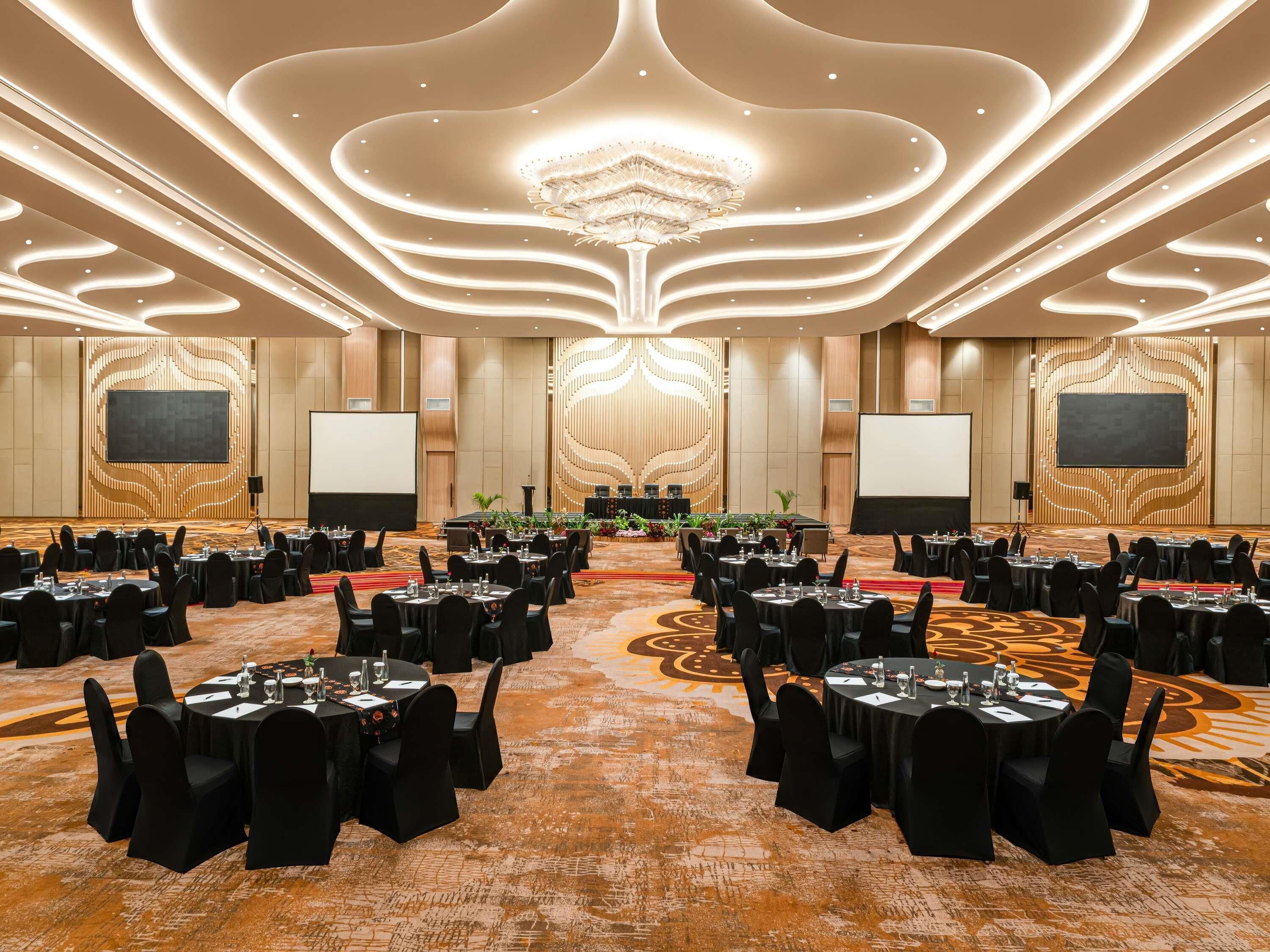 Un salón de conferencias con mesas redondas, sillas negras y un escenario central.