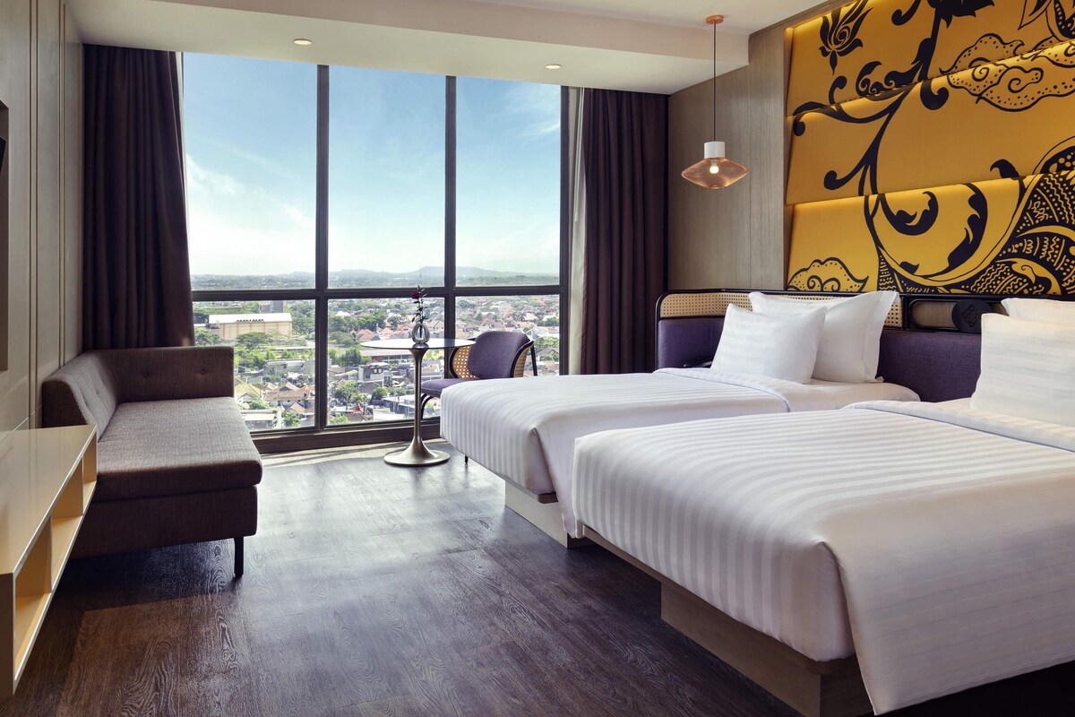 Habitación de hotel con un ventanal grande, dos camas, un sofá y una mesita.