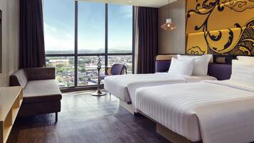 A hotel room with a large window, two beds, a sofa, and a small table.