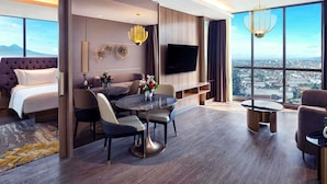 Una habitación de hotel moderna con una cama grande, una zona de comedor, un televisor y vistas a la ciudad.