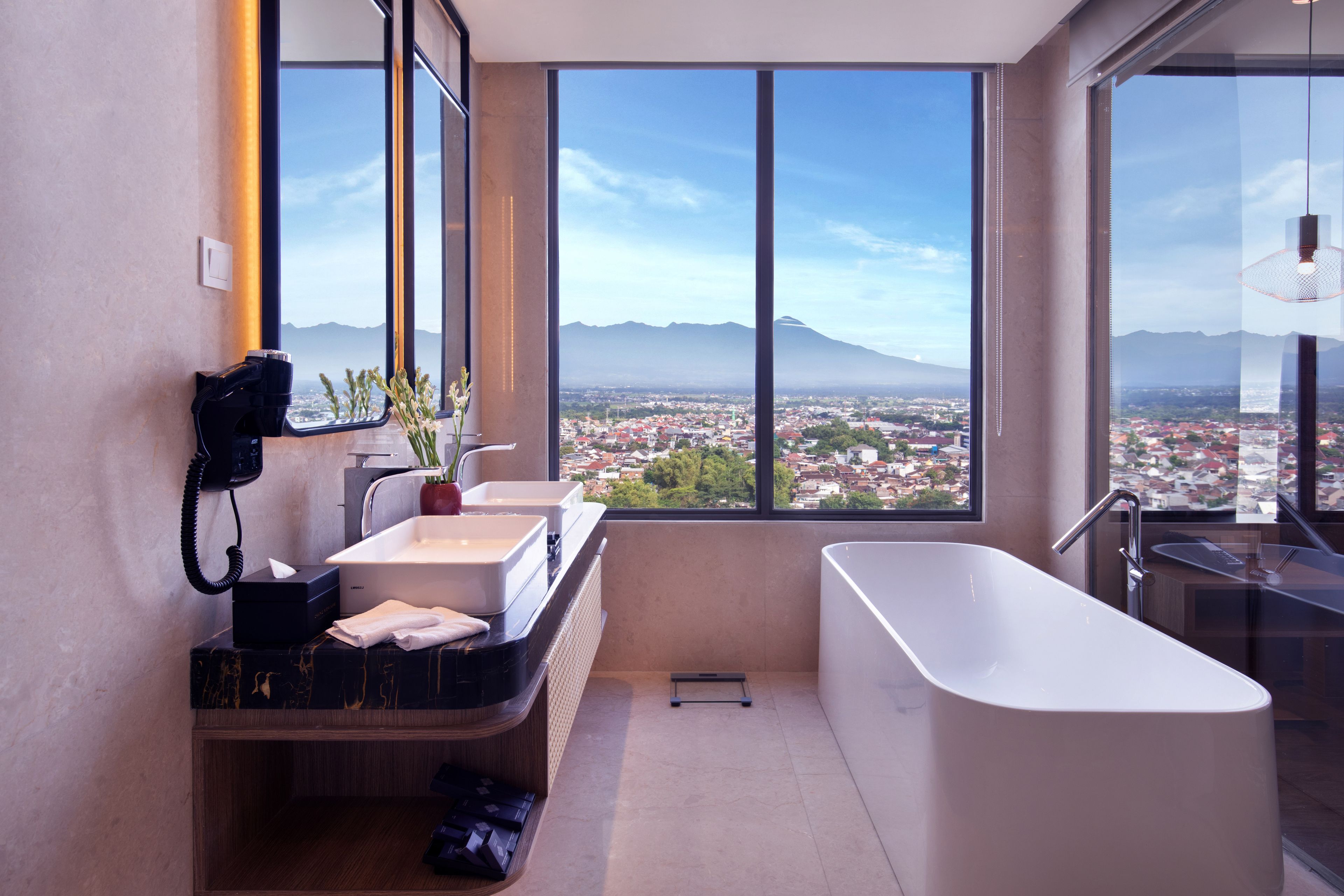 A modern bathroom with a large bathtub, two sinks, and a view of a cityscape through large windows.