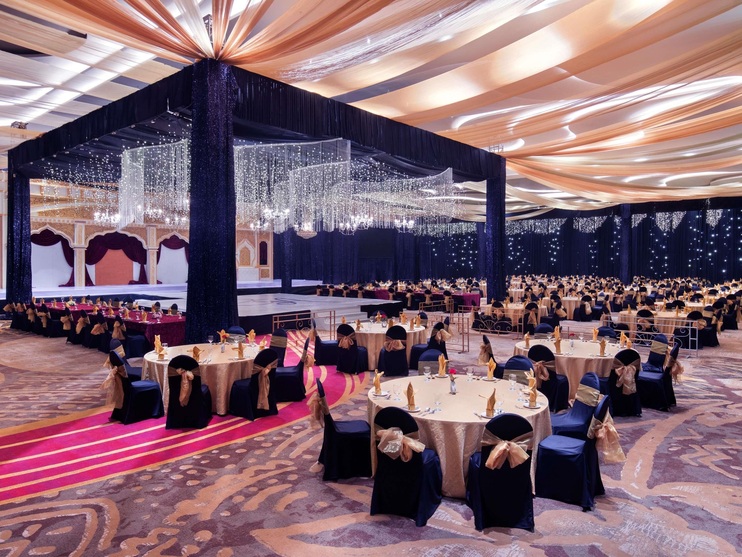Un salón de banquetes con mesas redondas, sillas y un escenario.
