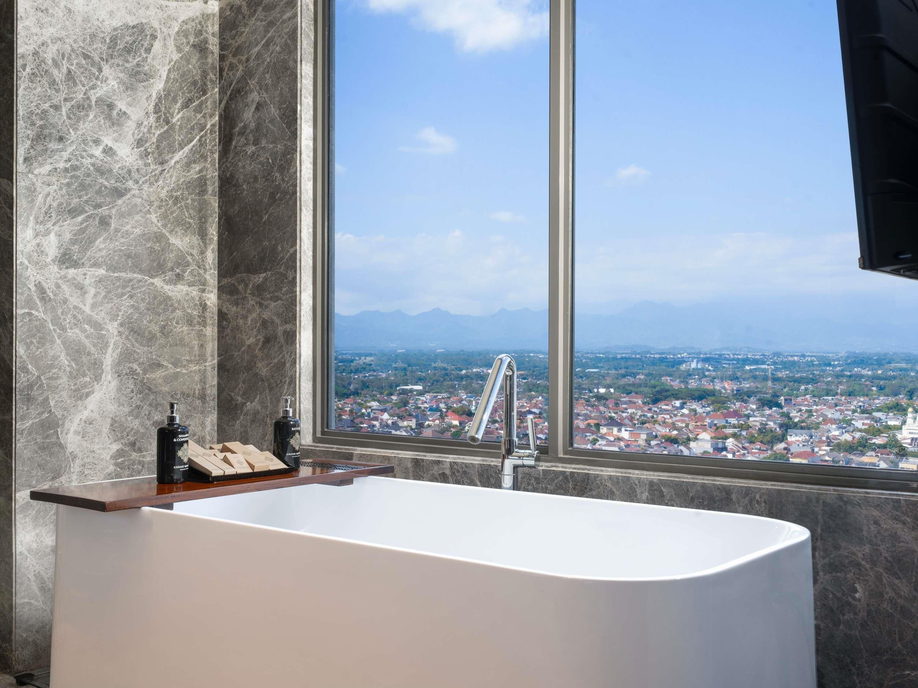 A modern bathroom with a freestanding bathtub, a large window with a city view, and marble walls.