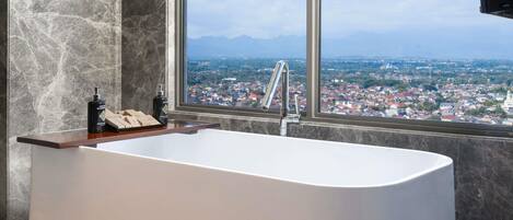 A modern bathroom with a freestanding bathtub, a large window with a city view, and marble walls.