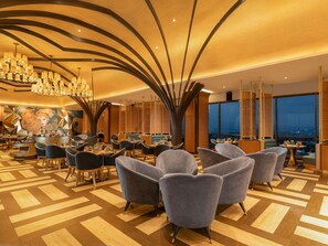 Un hall d’hôtel moderne avec un espace salon central, un bar et une grande fresque murale.
