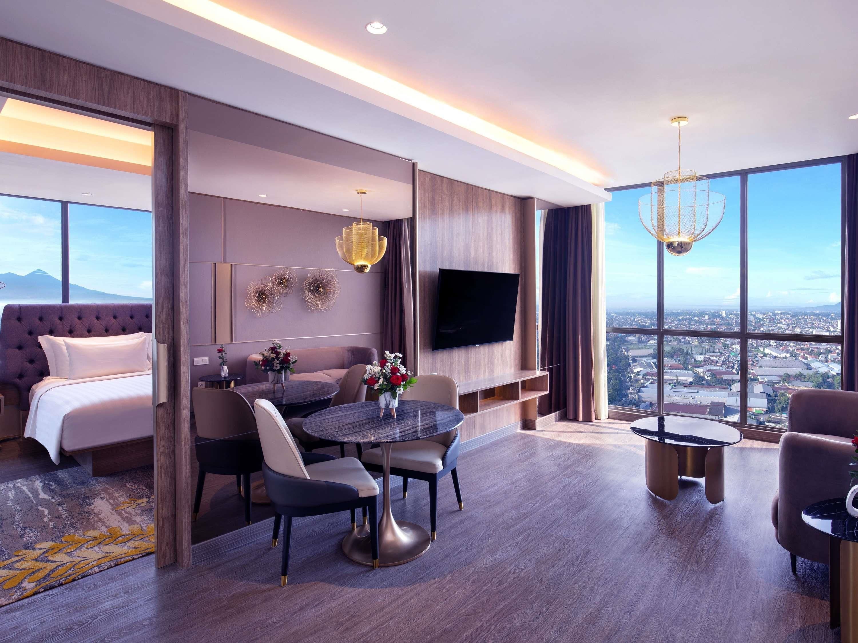 A modern hotel room with a large bed, a dining area, a TV, and a city view.
