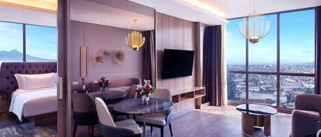 A modern hotel room with a large bed, a dining area, a TV, and a city view.