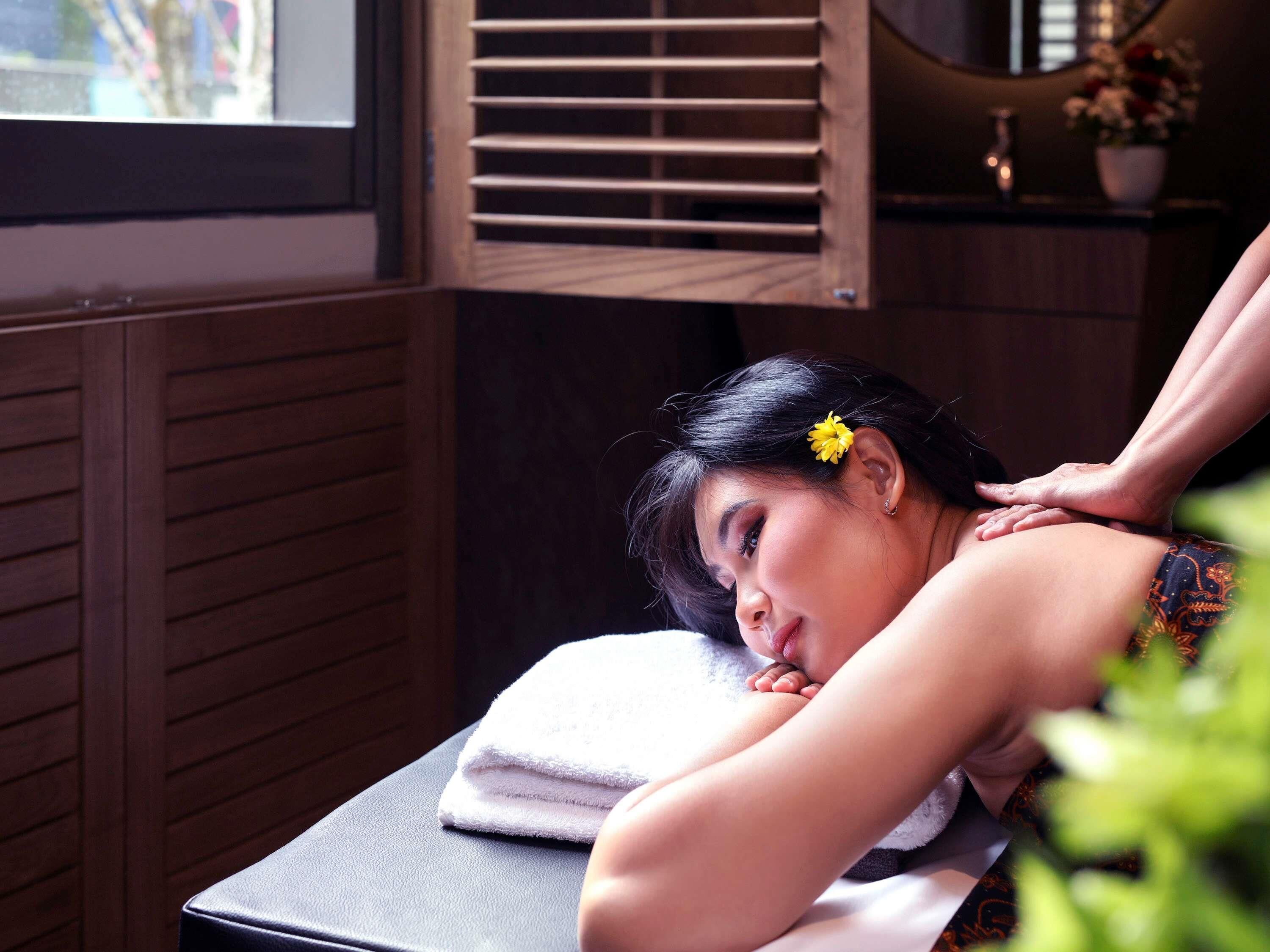 Een wellnessruimte met een massagetafel, houten lambrisering en een raam.