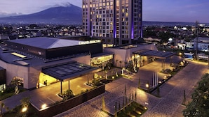 Un hotel con un llamativo letrero de 'Grand Mercure', una amplia zona de estacionamiento y una montaña al fondo.