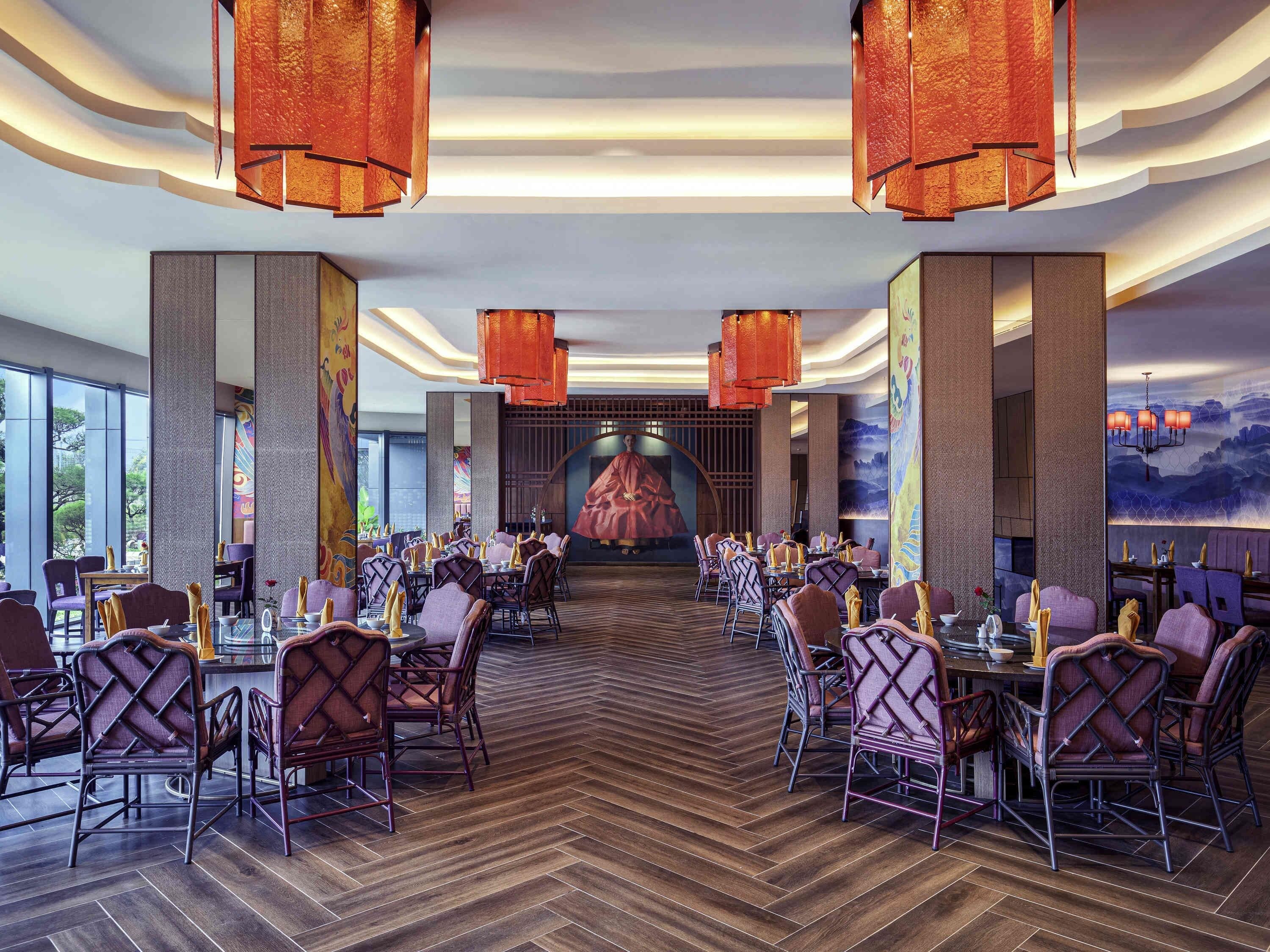 A spacious dining area with high tables and chairs, large windows, and a central mural.
