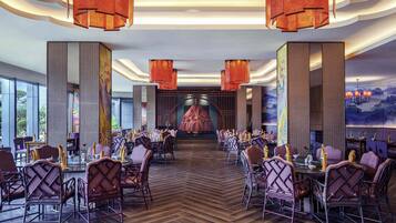 A spacious dining area with high tables and chairs, large windows, and a central mural.