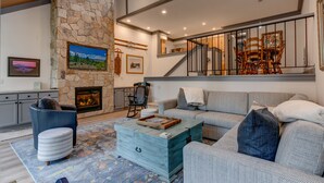 A spacious living room with a stone fireplace, a large sofa, a coffee table, and a staircase with a railing. - Esperanzas Lakeside Retreat: 3  BR, 2  BA Condominium in Tahoma, Sleeps 6 (Tahoma)