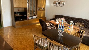 Ein Essbereich mit einem Holztisch, Stühlen und einer Couch. Im Hintergrund befindet sich eine Holzkommode mit Glastüren.